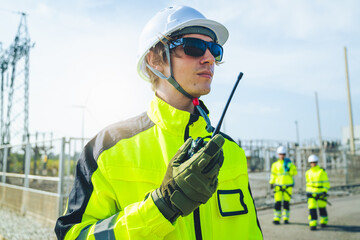 An engineer wearing safety gear closely inspects the base of a wind turbine in a renewable energy...