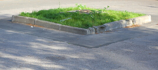 A small square lawn with a sewer manhole surrounded by a concrete curb