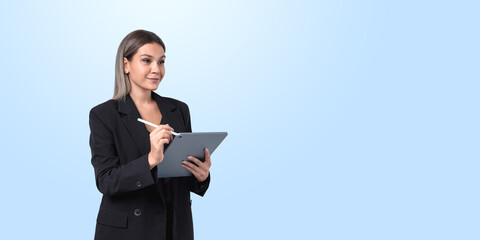 Woman in black suit holding tablet with stylus on light blue bac