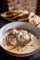 Shkmeruli, Georgian chicken in garlic cream sauce with red pepper flakes, served alongside freshly baked bread on a wooden tray.