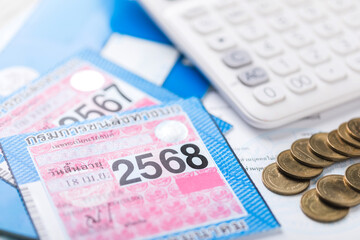 Thailand's 2025 vehicle tax sticker placed beside a calculator, emphasizing the importance of calculating and planning for annual vehicle tax payments and financial responsibilities