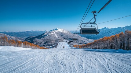Ski lift ascending snowy mountain slope with clear blue sky and autumnal trees.