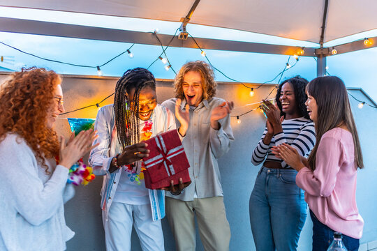 African man opening birthday gift with friends during roof party