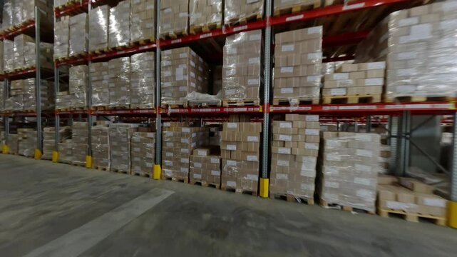 Tall steel shelves packed with cardboard boxes define warehouse interior. Boxes arranged in orderly manner making inventory management efficient FPV