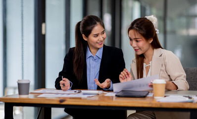 Two asian business women discuss financial management planning.standing and talking about analyzing documents in the workplace office
