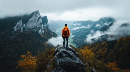 Adventurous Hiker Standing on Rocky Outcrop Overlooking Majestic Mountain Valley with Mist and Clouds in Expansive Autumn Landscape