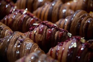 Close-up side view of various fresh baked brown croissants with different fillings and decorations on shelf of bakery or cafe. Soft focus. Copy space. Food and pastry background theme.