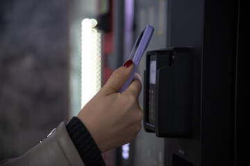 Close-up view of woman paying for purchase at free standing coffee vending machine using smartphone. Soft focus. Contactless and cashless payment theme.