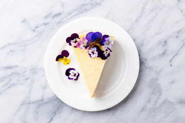 Cheesecake decorated with edible flowers on white plate. Marble background. Close up. Top view.