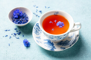 Cup of black tea with flowers. Blue background. Close up.