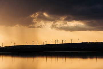 Fototapeta premium Wind turbines silhouetted against a sunset sky.