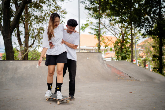 A young couple enthusiastically enjoying skateboarding lessons in a vibrant and sunny skate park - Powered by Adobe