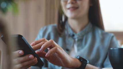 Close up of, young asian woman sitting at wooden table using mobile phone in coffee shop, front...