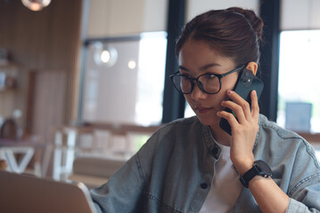 Asian business woman talking serious issue on mobile phone during working at coffee shop. Close up. Woman using smartphone thinking about problem solution