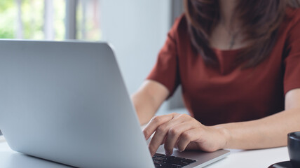 Fototapeta premium Woman working on laptop computer at home office. Business woman typing on notebook computer, surfing the net, searching the information, online working at home, closeup