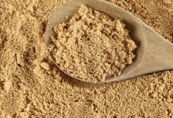 Brown unrefined sugar in wooden spoon , muscovado background and texture, top view