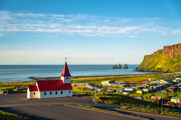 View of basalt stacks Reynisdrangar, black sand beach, church and city of Vik, Iceland