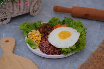 A vibrant meal consisting of red rice, meat, corn, carrots, lettuce, and a sunny side up egg