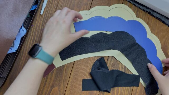 Women's hands lay out cloth and plastic base in form of ethnic Slavic crown on wooden table. Headdress from eco-leather and adhesive woven interlining fabric. Seamstress and her workplace.