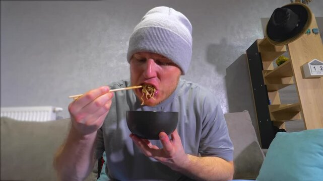 A young man eats pasta noodles with wooden chopsticks. Have dinner at home. Slow Motion