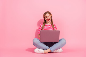 Young woman with braided hair and red lipstick uses a laptop against a pink background, embodying casual style and summer fashion.