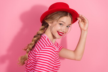 Charming young woman in striped top with vibrant red hat against pink background exudes youthful style and happiness