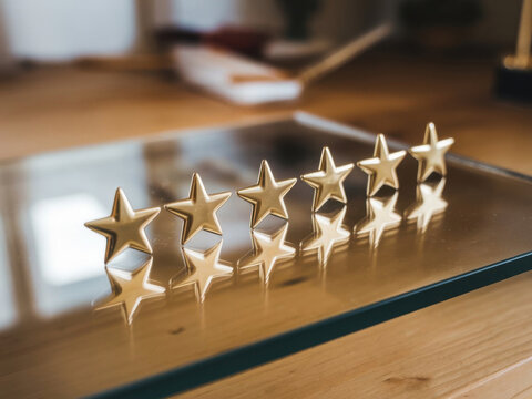 Cinco estrellas doradas dispuestas en fila, reflejadas en una superficie de vidrio
