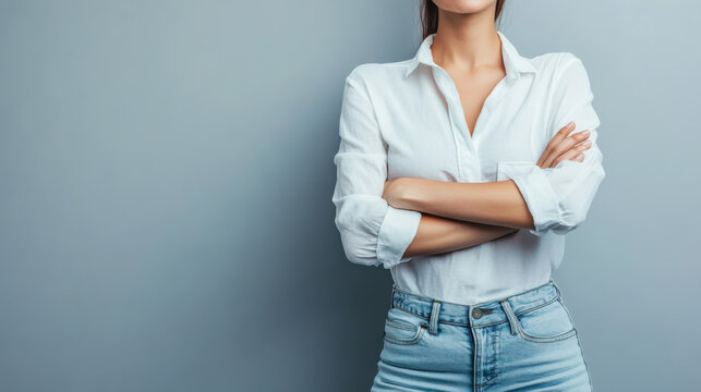Confident woman posing with crossed arms against a gray wall in a stylish outfit, showcasing a modern and professional look