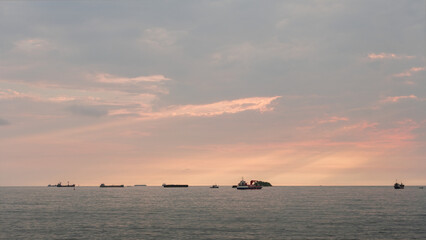 Naklejka premium A serene ocean sunset with multiple cargo ships on the horizon. The soft pastel sky and calm waters create a peaceful maritime scene, highlighting global shipping routes and evening coastal activity.