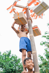 Obraz premium boy stands on friend's shoulders reaching for prize hanging during betel nut climbing competition