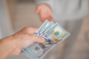 A hand passes hundred dollar bills to another person