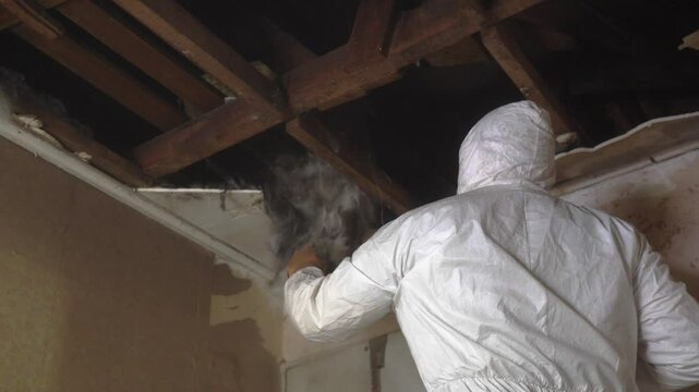 
man working in white overalls removing debris from the ceiling of a room