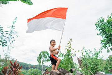 shirtless java boy raises the Indonesian flag while celebrating Indonesia's independence standing on a rock