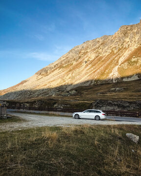 White BMW wagon in Lepontine Alps. Side view of BMW 5-series at sunset. Montespluga, Italy - September 21 2019.