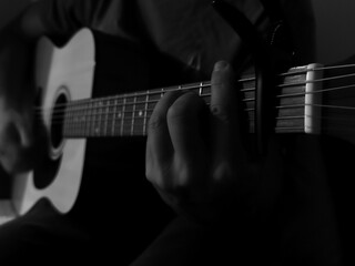 Guitarist playing acoustic guitar. Black and white photo of fingers on acoustic guitar strings
