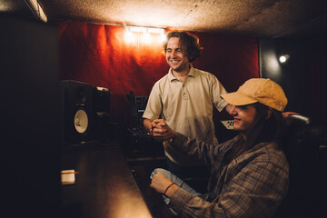 A musician and sound engineer, satisfied with their work, give each other a high five in a recording studio.