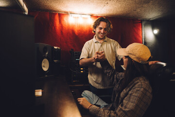 A musician and sound engineer, satisfied with their work, give each other a high five in a recording studio.