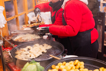vendor fries meat and sausage and potato on the grill in the city center at the Christmas market in...