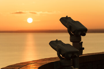 Binoculars on the terrace of Tihany Abbey. An amazing sunrise in the background, with the sun painting a golden line across Lake Balaton.