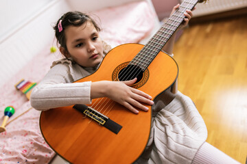 Fototapeta premium Little girl with autism plays guitar. Music therapy at home.
