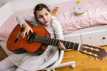 Little girl with autism plays guitar. Music therapy at home.