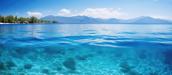 Fototapeta premium Crystal clear blue waters reflecting sunlight on a serene island with distant mountains under a clear blue sky