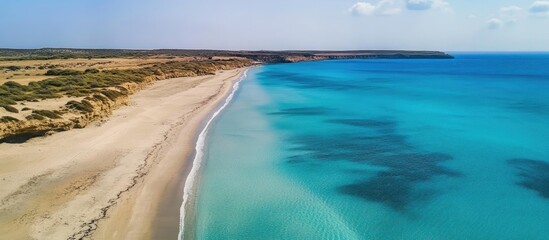Obraz premium Aerial view of Eagle Beach showcasing turquoise waters and sandy shoreline under a clear blue sky in a serene coastal landscape.