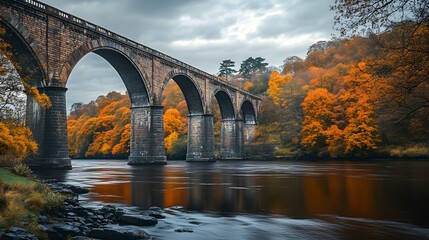Fototapeta premium A majestic stone bridge spanning a calm river surrounded by vibrant autumn foliage.