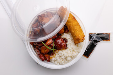 A plastic container of Chinese takeout featuring bourbon sauce-glazed chicken, white rice, and a spring roll.
