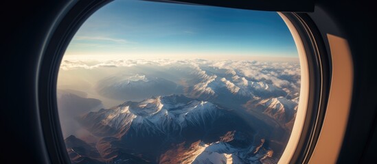 Aerial view of mountain summit through airplane window showcasing clouds and blue sky during sunrise or sunset