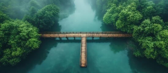 Fototapeta premium Aerial view of a serene river and wooden bridge surrounded by lush greenery and misty landscape in a tranquil natural setting