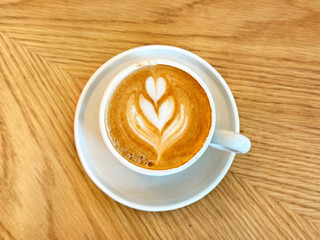 Coffee latte with coffee leaves art served on a white cup isolated on a rustic bright wooden table. 