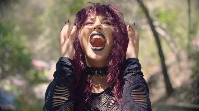 A gothic style girl with wavy reddish hair and dramatic makeup screams and shakes her head violently, as if in anger, rage or despair, creating an unsettling appearance. Metaphor of madness and frenzy