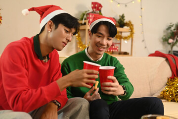 Two friends in festive outfits clink their red cups with warm smiles, sharing a joyful moment in a cozy Christmas party on a holiday